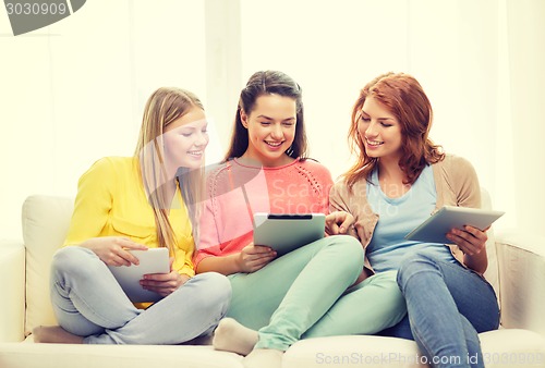 Image of three smiling teenage girls with tablet pc at home