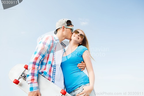 Image of smiling couple with skateboard kissing outdoors