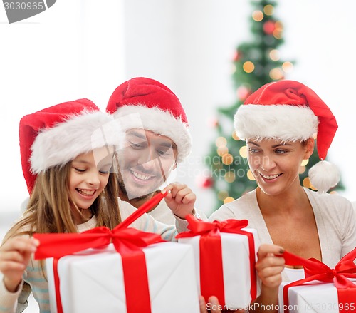 Image of happy family in santa hats sitting with gift boxes