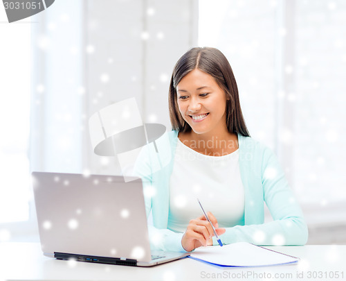 Image of smiling young woman with laptop and notebook