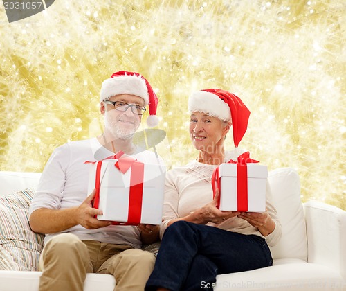 Image of happy senior couple in santa hats with gift boxes