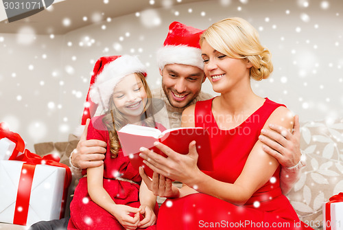 Image of smiling family in santa hats reading book at home