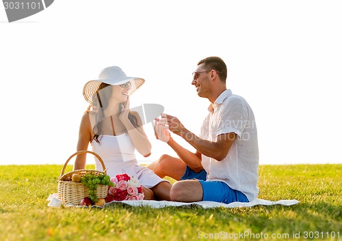 Image of smiling couple with small red gift box on picnic