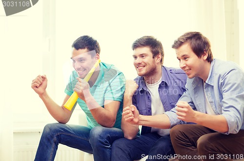 Image of happy male friends with vuvuzela watching sports