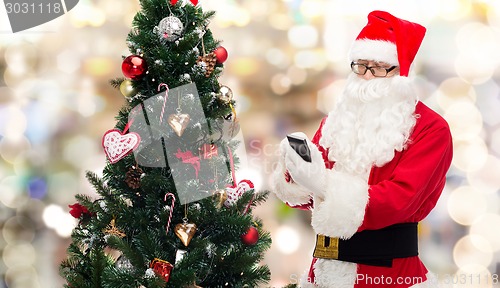 Image of santa claus with smartphone and christmas tree