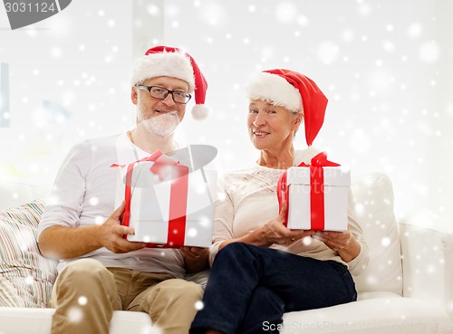 Image of happy senior couple in santa hats with gift boxes