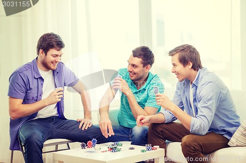 Image of happy three male friends playing poker at home