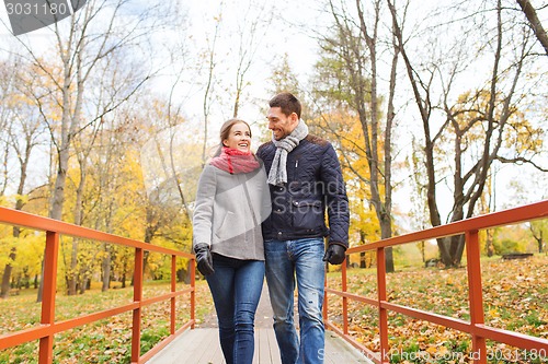 Image of smiling couple hugging on bridge in autumn park