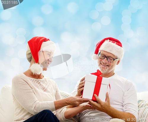 Image of happy senior couple in santa hats with gift box