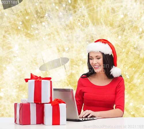 Image of smiling woman in santa hat with gifts and laptop