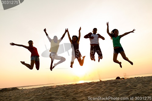 Image of smiling friends dancing and jumping on beach