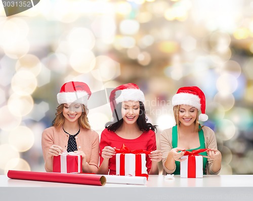 Image of smiling women in santa helper hats packing gifts