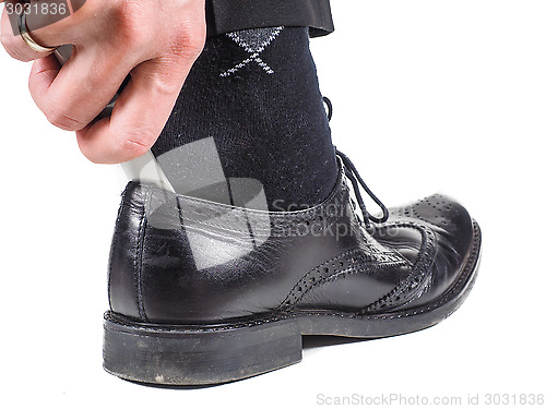 Image of Male hand entering foot with black sock into black leather shoe 