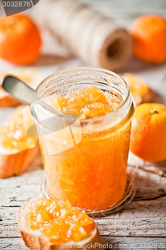 Image of orange jam in glass jar, tangerines and bread 