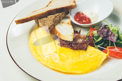 Image of Omelet with bacon served on white plate, vegetables aside