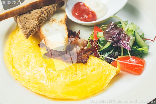 Image of Omelet with bacon served on white plate, vegetables aside