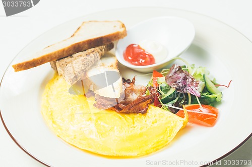 Image of Omelet with bacon served on white plate, vegetables aside