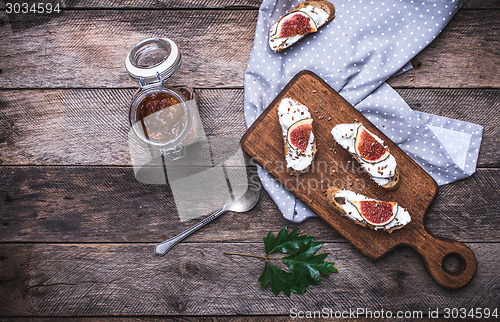 Image of Sliced figs, jam and Bruschetta on choppingboard in rustic style