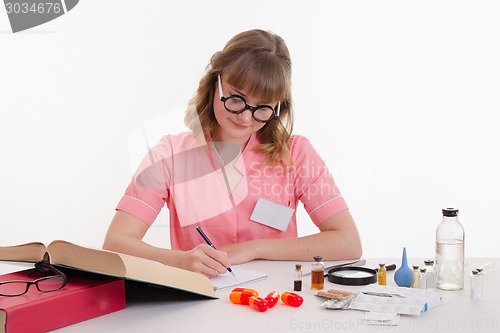 Image of Pharmacist reading guide writes notes in a notebook