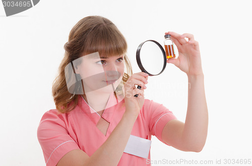 Image of Pharmacist surprise considering liquid through a magnifying glass