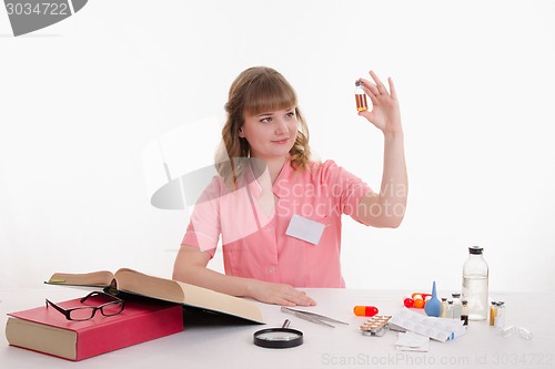 Image of Pharmacist looking liquid in vial, sitting at table