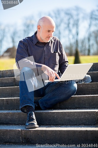 Image of Man sitting on a bench using a laptop