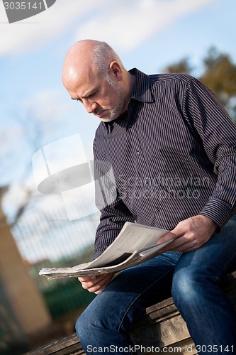 Image of Man sitting reading a newspaper on a stone wall