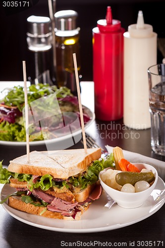 Image of Delicious pastrami club sandwich and pickles