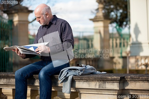 Image of Man sitting reading a newspaper on a stone wall