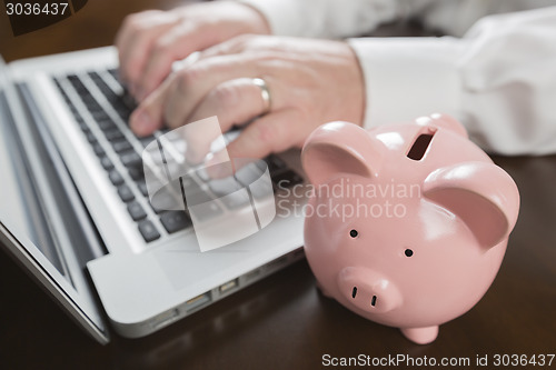 Image of Piggy Bank Near Male Hands Typing on Laptop