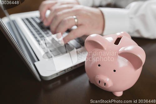 Image of Piggy Bank Near Male Hands Typing on Laptop
