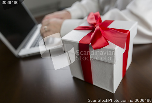 Image of White Gift Box with Red Bow Near Man using Laptop