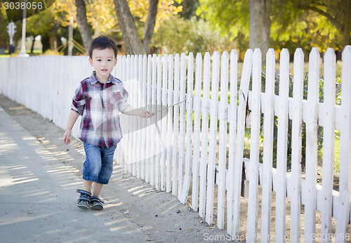 Image of Young Mixed Race Boy Walking with Stick Along White Fence