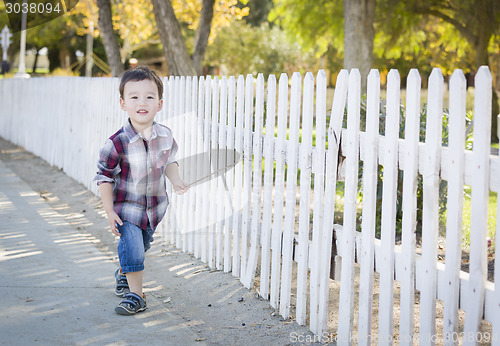 Image of Young Mixed Race Boy Walking with Stick Along White Fence