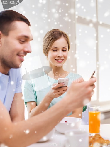 Image of smiling couple with smartphones having breakfast