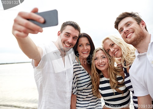 Image of happy friends on beach and taking selfie