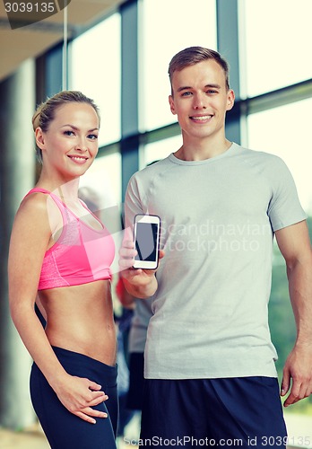 Image of smiling young woman with personal trainer in gym