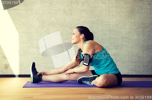 Image of smiling woman stretching leg on mat in gym