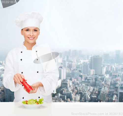 Image of smiling female chef spicing vegetable salad