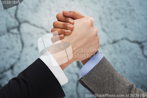 Image of close up of hands arm wrestling over concrete wall