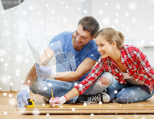 Image of smiling couple measuring wood flooring