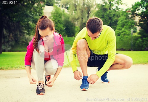 Image of smiling couple tying shoelaces outdoors