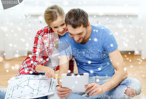 Image of smiling couple with tablet and blueprint at home