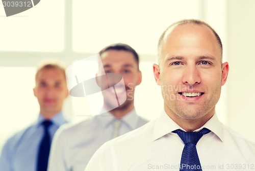 Image of smiling businessman in office with team on back