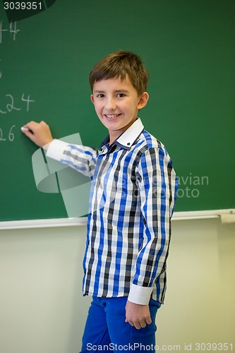 Image of little smiling schoolboy writing on chalk board