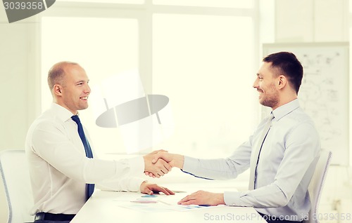 Image of two smiling businessmen shaking hands in office