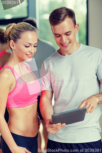 Image of smiling young woman with personal trainer in gym