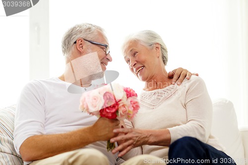 Image of happy senior couple with bunch of flowers at home