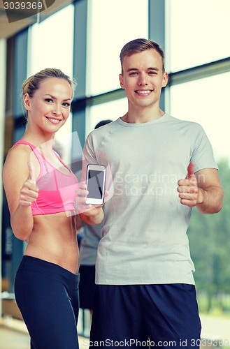 Image of smiling young woman with personal trainer in gym