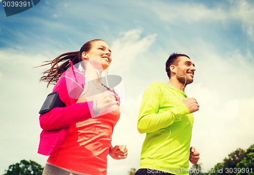 Image of smiling couple with earphones running outdoors